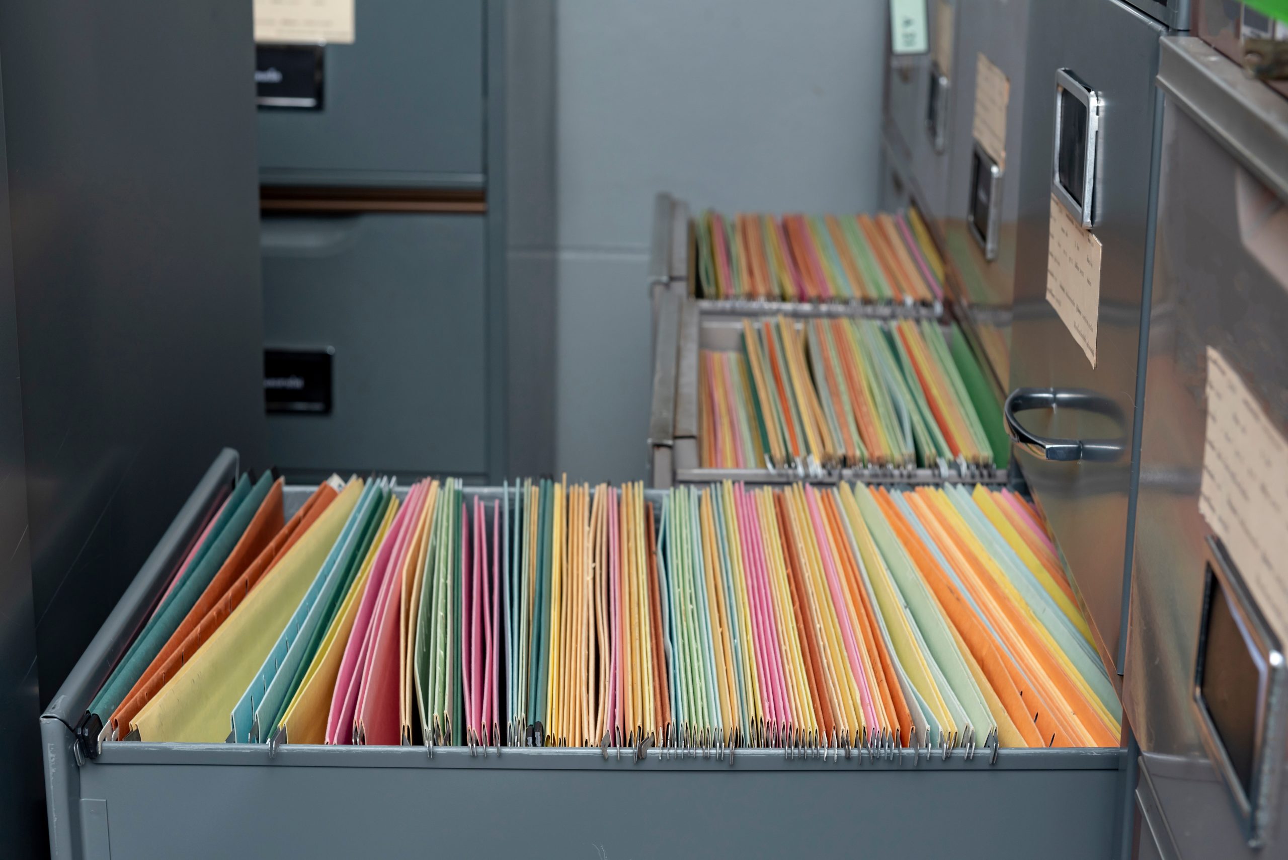 Open filing cabinets filled with colorful paper folders, representing the outdated systems colleges are replacing with paperless solutions.