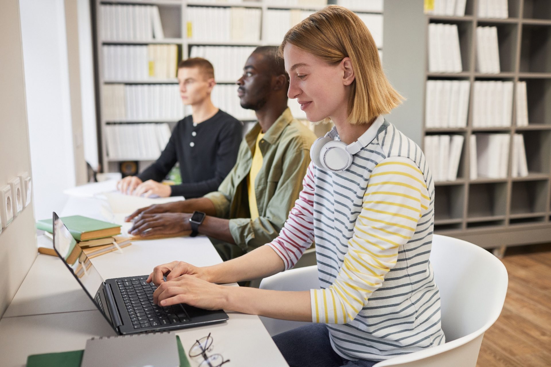 Students studying in a library, with one using a laptop and another with a braille book, representing accessible education in practice.