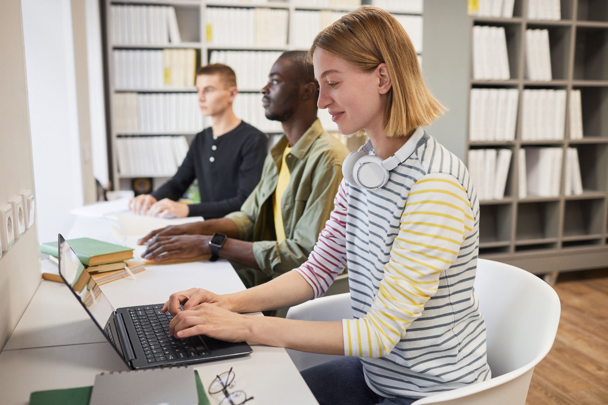 Students studying in a library, with one using a laptop and another with a braille book, representing accessible education in practice.