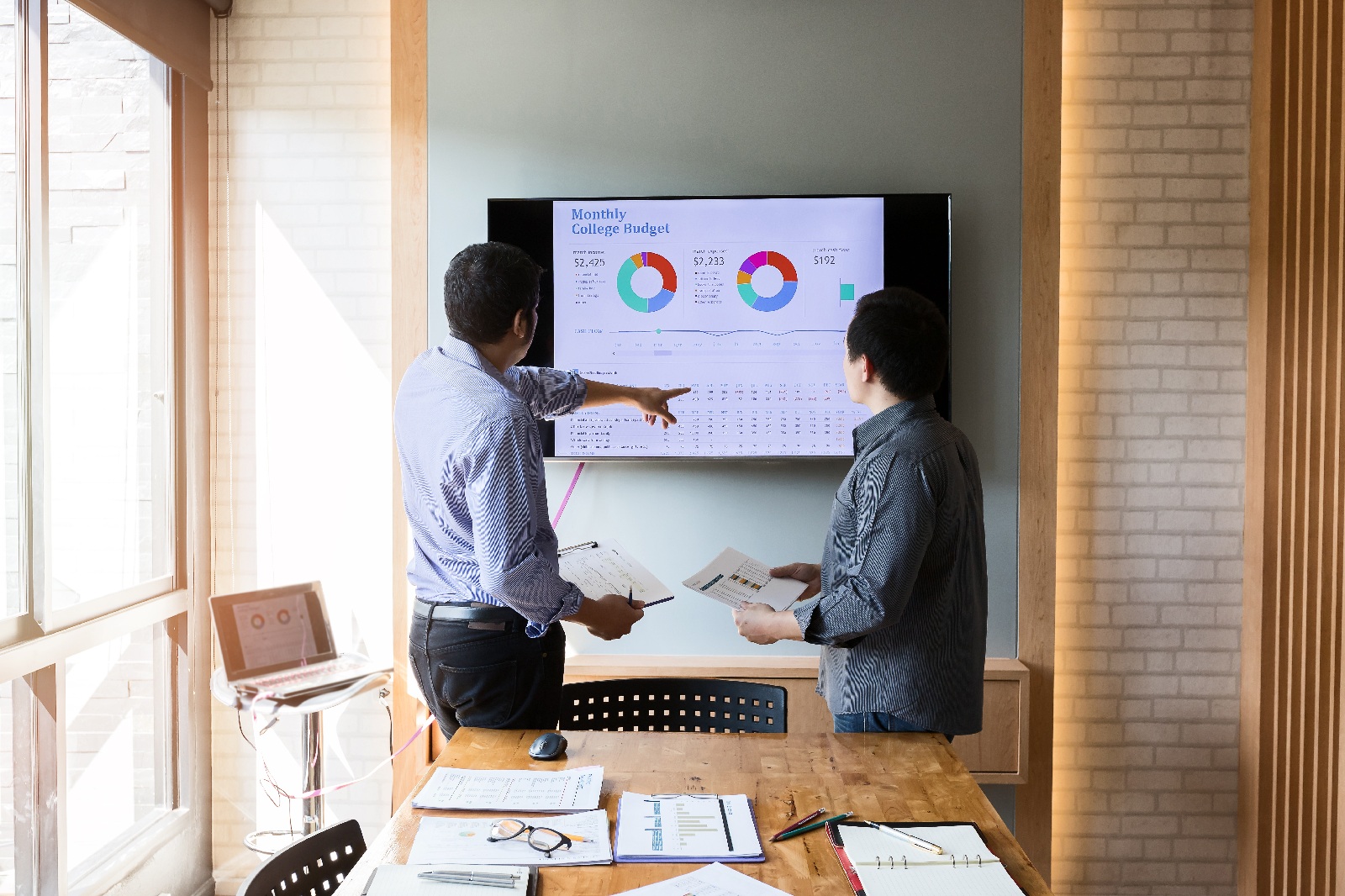 Two staff review charts on a screen during a meeting.