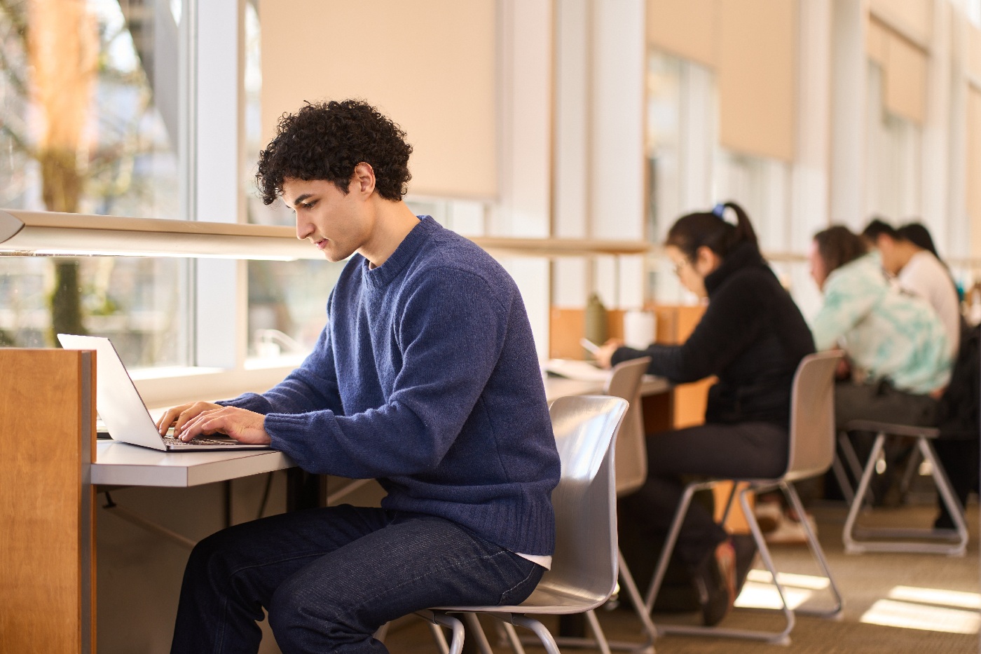 Student using a laptop at a study desk in a bright campus library.